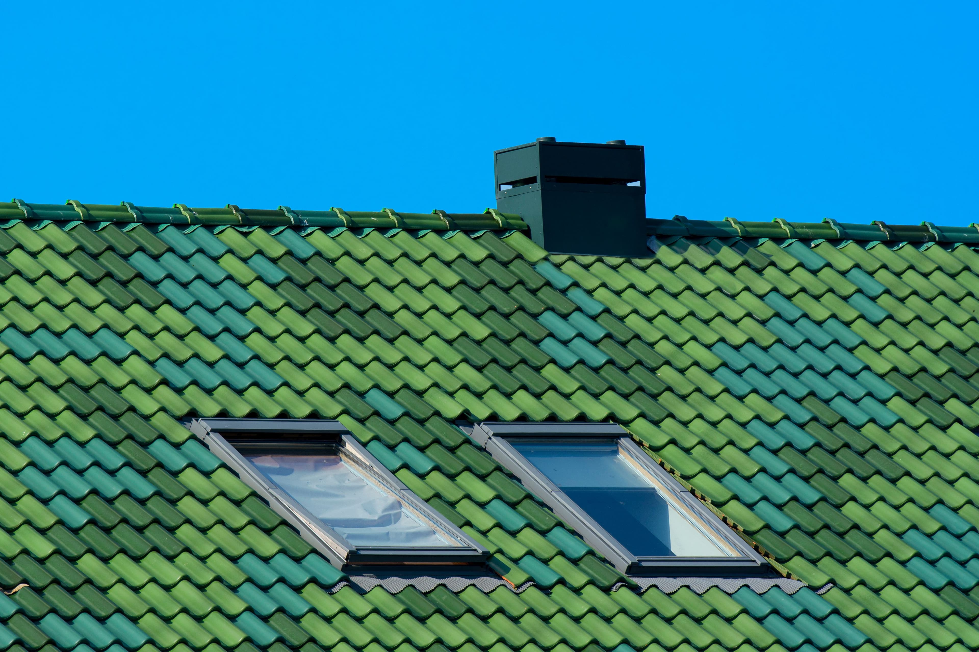 Close-up of green roof tiles with skylights under a clear blue sky